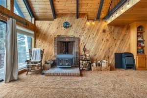 Interior space with a wood stove, vaulted ceiling with beams, wooden ceiling, and wood walls