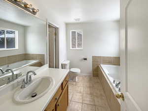 Bathroom featuring tile patterned floors, toilet, vanity, and tiled tub