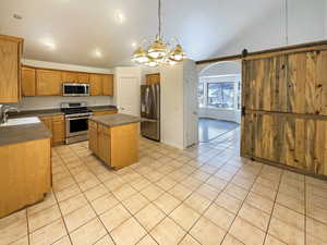 Kitchen with stainless steel appliances, a center island, a barn door, decorative light fixtures, and sink