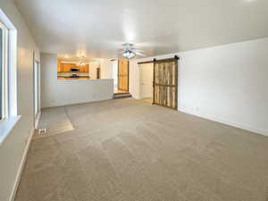 Unfurnished living room featuring ceiling fan, a barn door, and light colored carpet