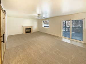 Unfurnished living room with light carpet, a tiled fireplace, ceiling fan, and a barn door