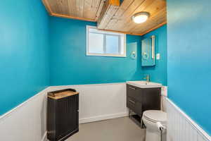 Bathroom featuring toilet, vanity, wooden ceiling, and concrete floors