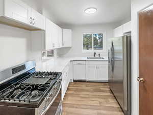 Kitchen with appliances with stainless steel finishes, sink, white cabinetry, and light wood-type flooring