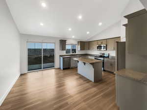 Kitchen featuring appliances with stainless steel finishes, dark wood-type flooring, a center island, sink, and dark stone countertops