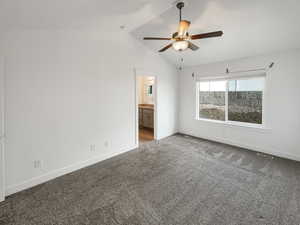 Unfurnished bedroom featuring dark carpet, vaulted ceiling, ceiling fan, and connected bathroom