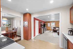 Kitchen with stainless steel dishwasher, pendant lighting, wood walls, and light colored carpet