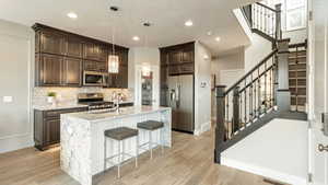 Kitchen featuring an island with sink, decorative light fixtures, sink, light stone counters, and appliances with stainless steel finishes