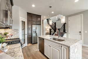 Kitchen with sink, light wood-type flooring, stainless steel appliances, light stone countertops, and a kitchen island with sink