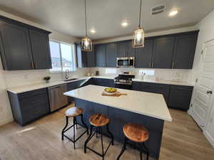 Kitchen featuring a kitchen bar, appliances with stainless steel finishes, sink, pendant lighting, and a kitchen island