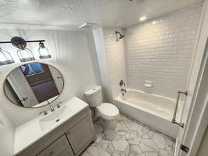 Full bathroom featuring toilet, tiled shower / bath combo, vanity, and a textured ceiling