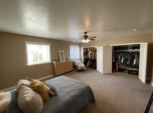 Carpeted bedroom with a textured ceiling, two closets, and ceiling fan