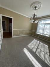 Carpeted spare room with a notable chandelier and ornamental molding