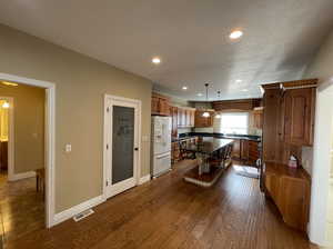 Kitchen featuring white refrigerator with ice dispenser, hanging light fixtures, a center island, dark hardwood / wood-style flooring, and sink