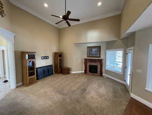 Unfurnished living room with a towering ceiling, ceiling fan, light carpet, a fireplace, and ornamental molding