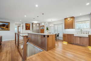 Kitchen featuring sink, backsplash, light wood-type flooring, a kitchen island, and hanging light fixtures