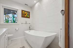 Bathroom featuring vanity, toilet, and a tub to relax in