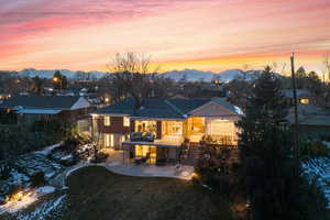 Back house at dusk featuring a mountain view, a patio, and a lawn