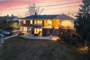 Back house at dusk with a patio area, a yard, and a balcony