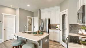 Kitchen with a center island with sink, sink, light stone counters, stainless steel appliances, and white cabinets