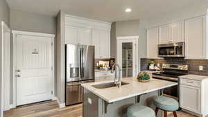 Kitchen with appliances with stainless steel finishes, sink, white cabinets, an island with sink, and light stone countertops