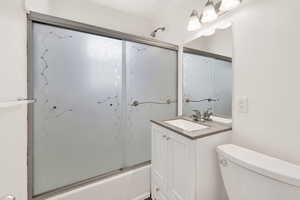 Full bathroom with combined bath / shower with glass door, vanity, and toilet