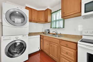 Laundry area with sink, dark wood-type flooring, and stacked washer / drying machine