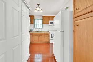 Kitchen with sink, white appliances, an inviting chandelier, and wood-type flooring