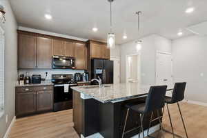 Large kitchen island with single basin sink, black stainless-steel appliances, granite countertops, large pantry, and powder bathroom