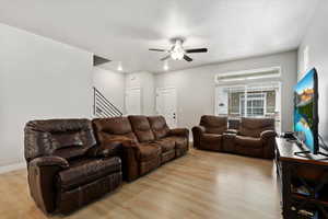 Living room featuring light wood style laminate flooring, large windows, and ceiling fan