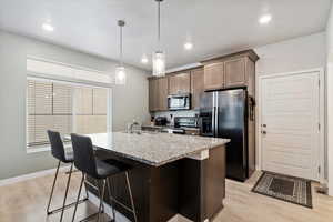 Large kitchen island with single basin sink, black stainless-steel appliances, granite countertops, and pendant lighting