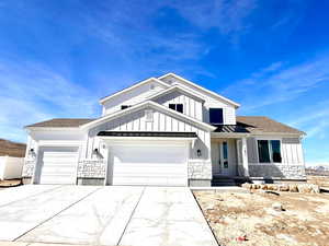 View of front facade with stone siding, a garage, board and batten siding, and driveway
