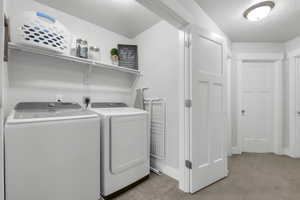 Laundry room featuring a textured ceiling, light carpet, and separate washer and dryer