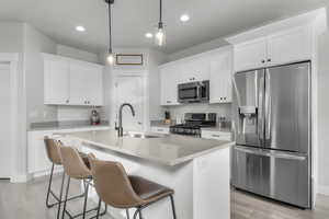 Kitchen featuring a center island with sink, stainless steel appliances, white cabinets, decorative light fixtures, and sink