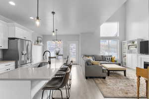 Kitchen with white cabinetry, hanging light fixtures, light hardwood / wood-style flooring, stainless steel fridge, and sink