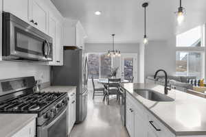 Kitchen featuring appliances with stainless steel finishes, white cabinets, decorative light fixtures, light hardwood / wood-style floors, and sink