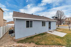 Rear view of house with a shingled roof, stucco siding, a yard, and fence