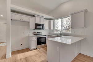 Kitchen featuring electric range, light wood-type flooring, white cabinets, and kitchen peninsula