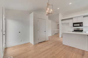 Kitchen with an inviting chandelier, light hardwood / wood-style flooring, white cabinetry, decorative light fixtures, and stainless steel range with electric cooktop