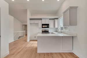 Kitchen with stainless steel range with electric stovetop, sink, kitchen peninsula, and light wood-type flooring