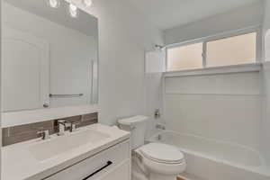 Full bathroom with washtub / shower combination, backsplash, vanity, and toilet