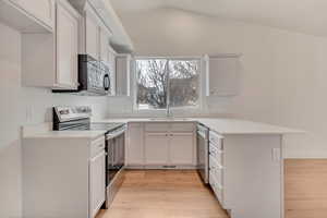 Kitchen featuring stainless steel appliances, white cabinets, lofted ceiling, sink, and kitchen peninsula