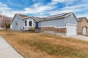 Ranch-style home featuring a garage, roof mounted solar panels, a front lawn, and stucco siding