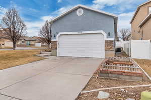 View of side of home featuring an attached garage, fence, stone siding, concrete driveway, and stucco siding