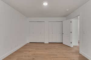 Unfurnished bedroom with light wood-type flooring and two closets