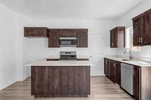 Kitchen with sink, appliances with stainless steel finishes, a center island, and light hardwood / wood-style flooring