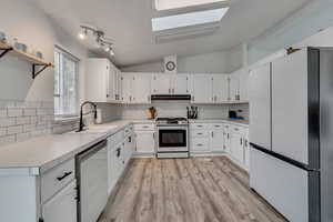 Kitchen with appliances with stainless steel finishes, sink, white cabinets, lofted ceiling with skylight, and decorative backsplash