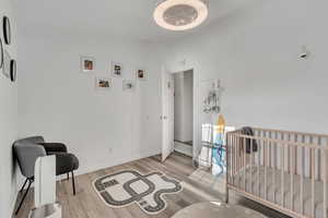 Bedroom with light hardwood / wood-style floors, a crib, and lofted ceiling