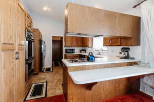 Kitchen featuring a breakfast bar area, stainless steel appliances, kitchen peninsula, and lofted ceiling