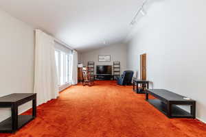 Interior space with track lighting, vaulted ceiling, and carpet flooring