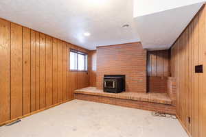 Unfurnished living room featuring a wood stove, wooden walls, and a textured ceiling